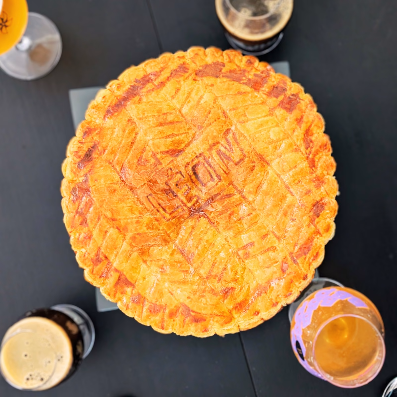 Galette des rois dorée gravée LÉON, entourée de verres de bière blonde et de bière noire.